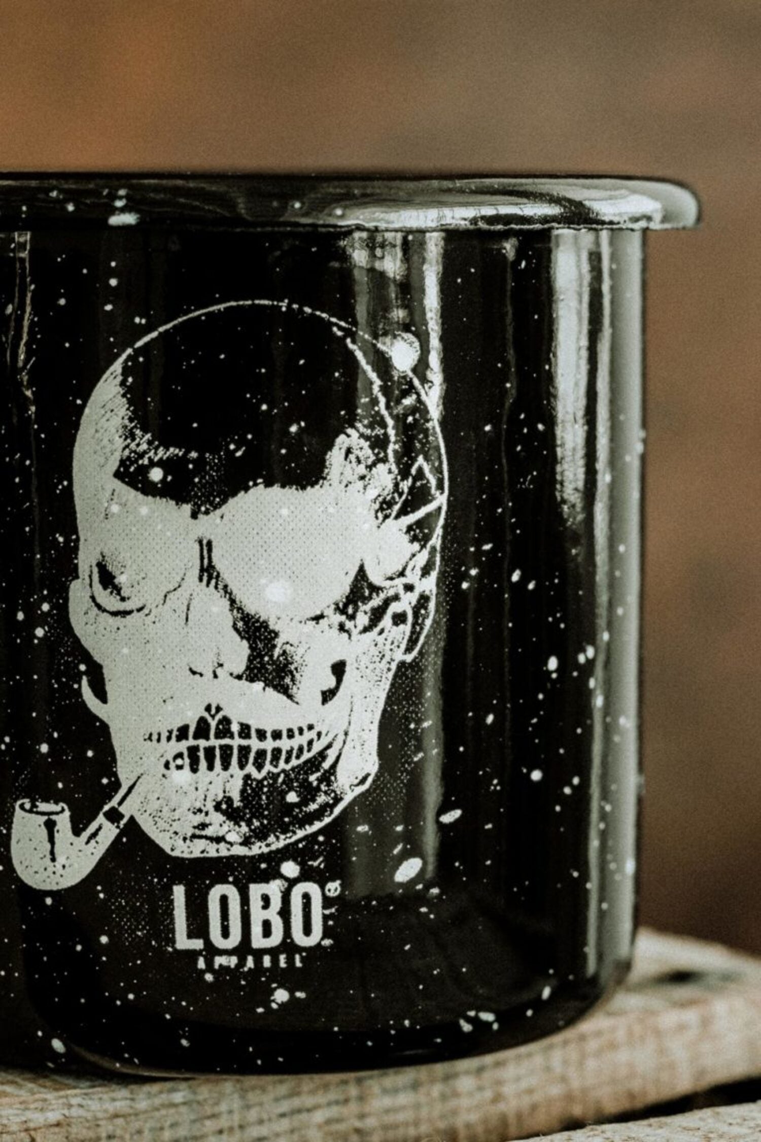 Close-up of the black Lobo Skull Enamel mug, highlighting the speckled enamel texture and the detailed illustration of a skull with a pipe.