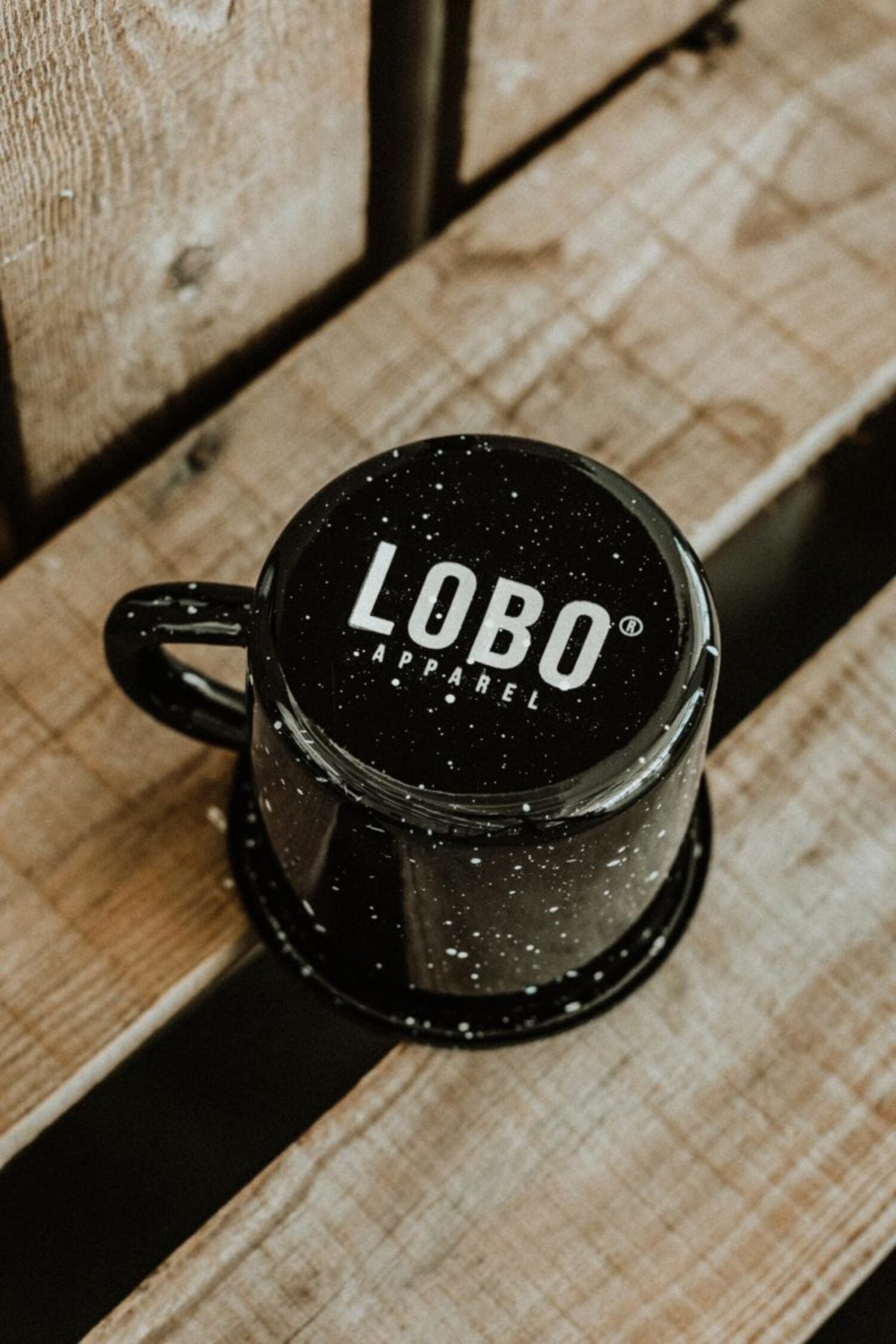 Top view of the inverted black Lobo Skull Enamel mug, revealing the Lobo Apparel logo on the base over a wooden surface.