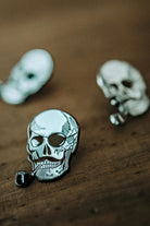 Artistic close-up of the Lobo Skull metal pin featuring a skull with a mustache and pipe design, focused on a rustic wooden surface.