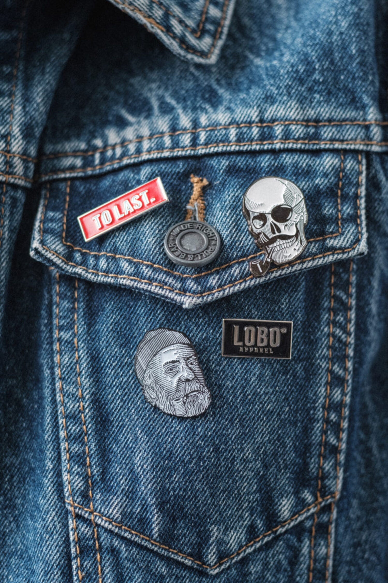 Denim jacket customized with Lobo Apparel pins, featuring the Lobo Skull and the red "To Last" enamel pin.