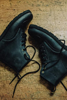 Pair of black leather Lobo Tigre Boots 3rd Edition on wood, showing the motorcycle shifter protection reinforcement and golden eyelets.