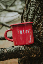 Lobo "To Last" red enamel mug resting on a textured tree branch.