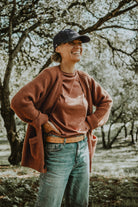 Smiling woman outdoors wearing the Lobo "To Last" grey denim cap, paired with a rust-colored cardigan.