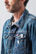 Man wearing a denim jacket with a set of Lobo Apparel metal pins on the front pocket, including the red To Last pin.