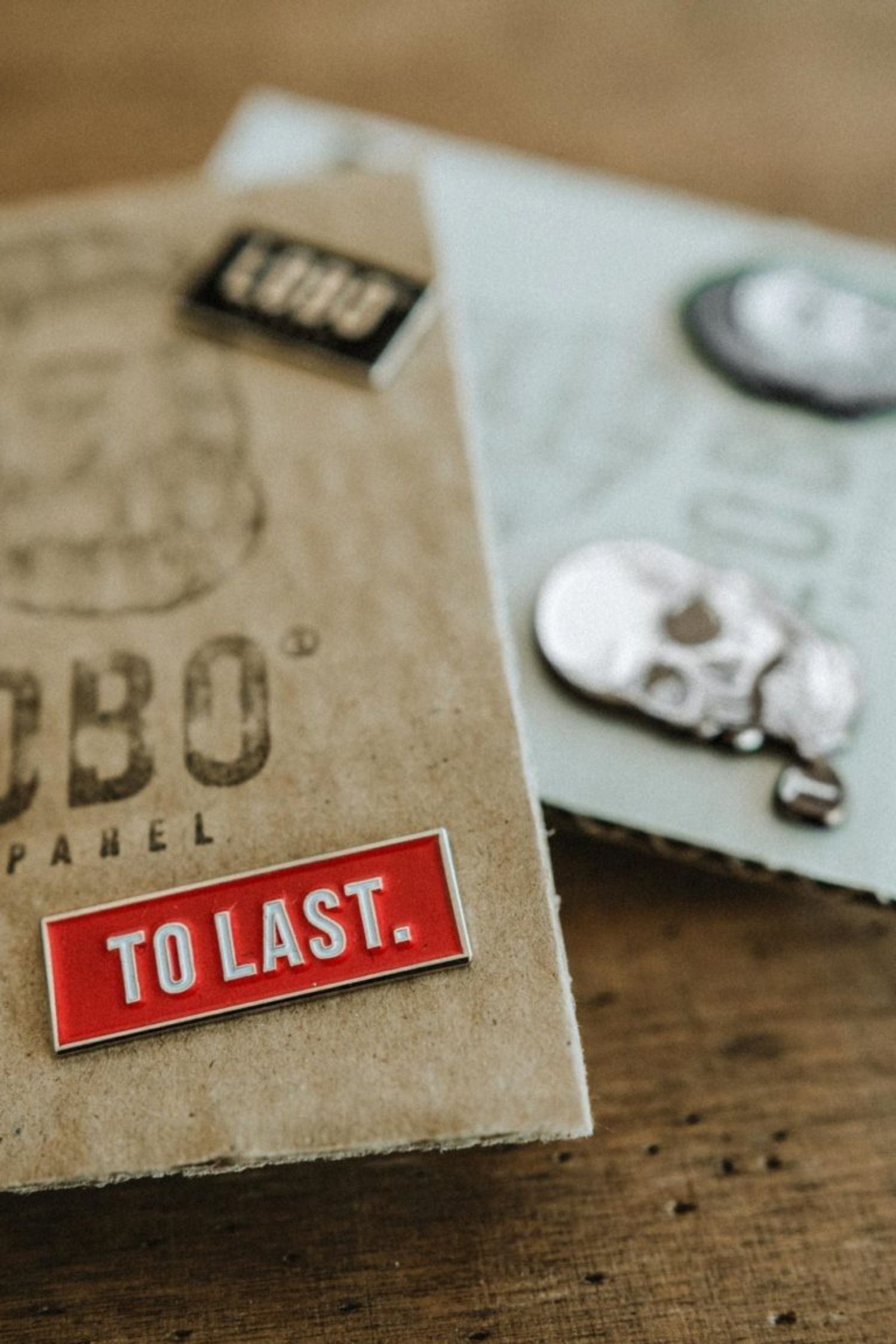 Red Lobo To Last metal pin resting on a Lobo Apparel kraft packaging, with other collection pins visible in the background.