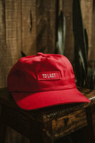 Red premium LOBO Apparel cap with an embroidered "TO LAST" patch on the front, set on a rustic wooden surface.