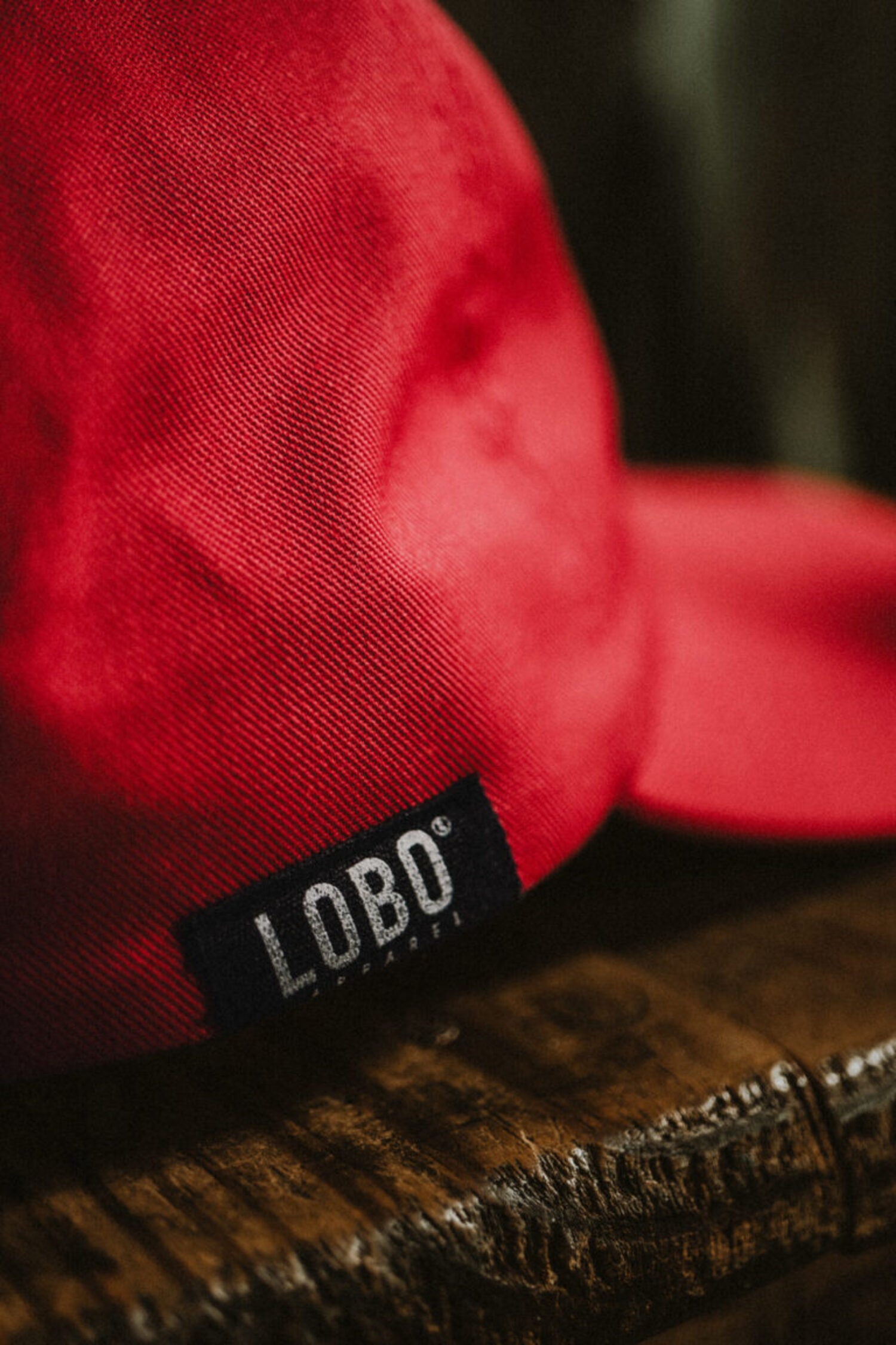 Close-up of the black side tab featuring the LOBO Apparel logo on a high-quality red twill cap.