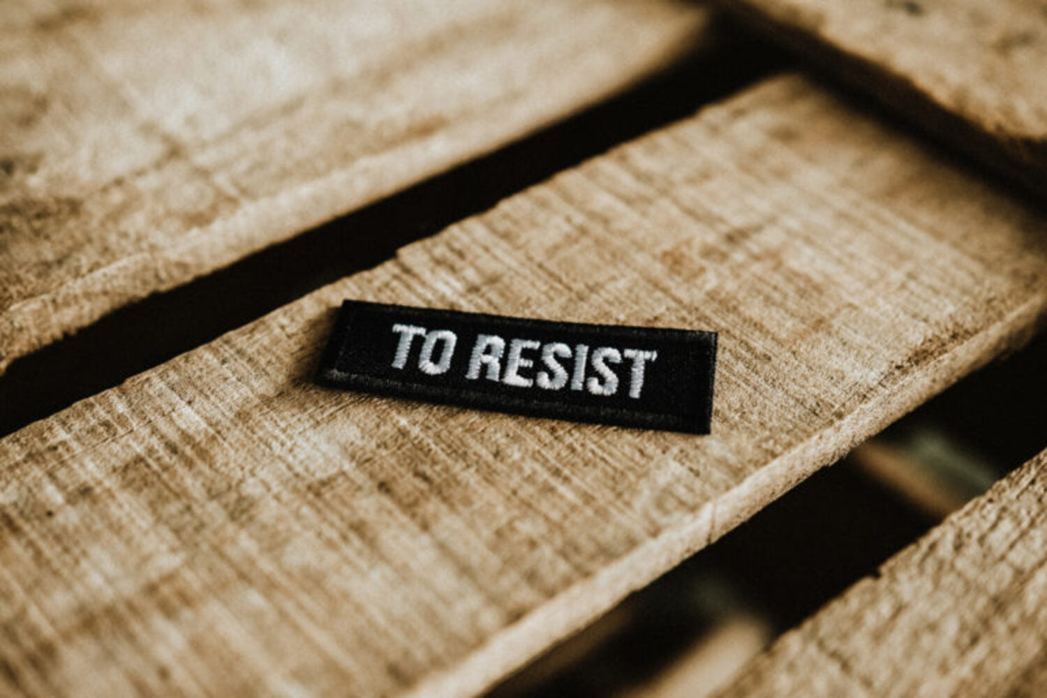 Lobo To Resist black and white embroidered patch (6x2 cm) on wood, iron-on or sew-on clothing accessory.