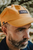 Front close-up of a bearded man wearing the Lobo "To Resist" yellow cap, showcasing the unisex design and fit.