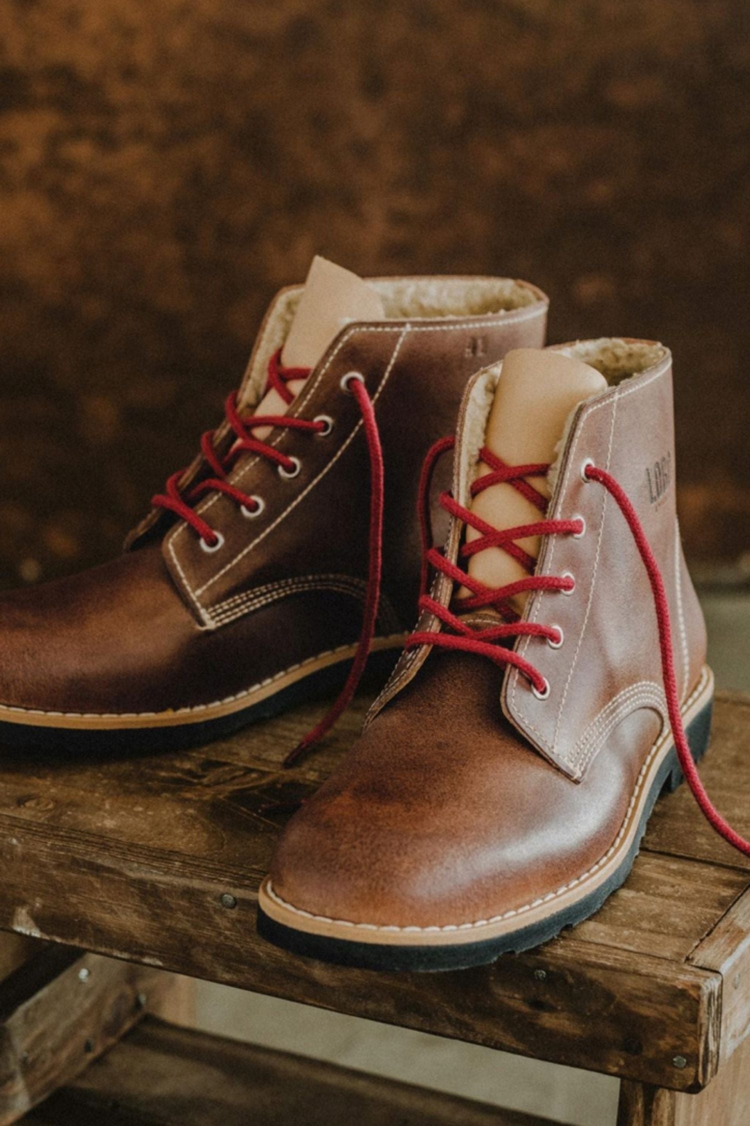 Lobo Warm Boots in brown leather featuring red laces and wool lining on a wooden bench.