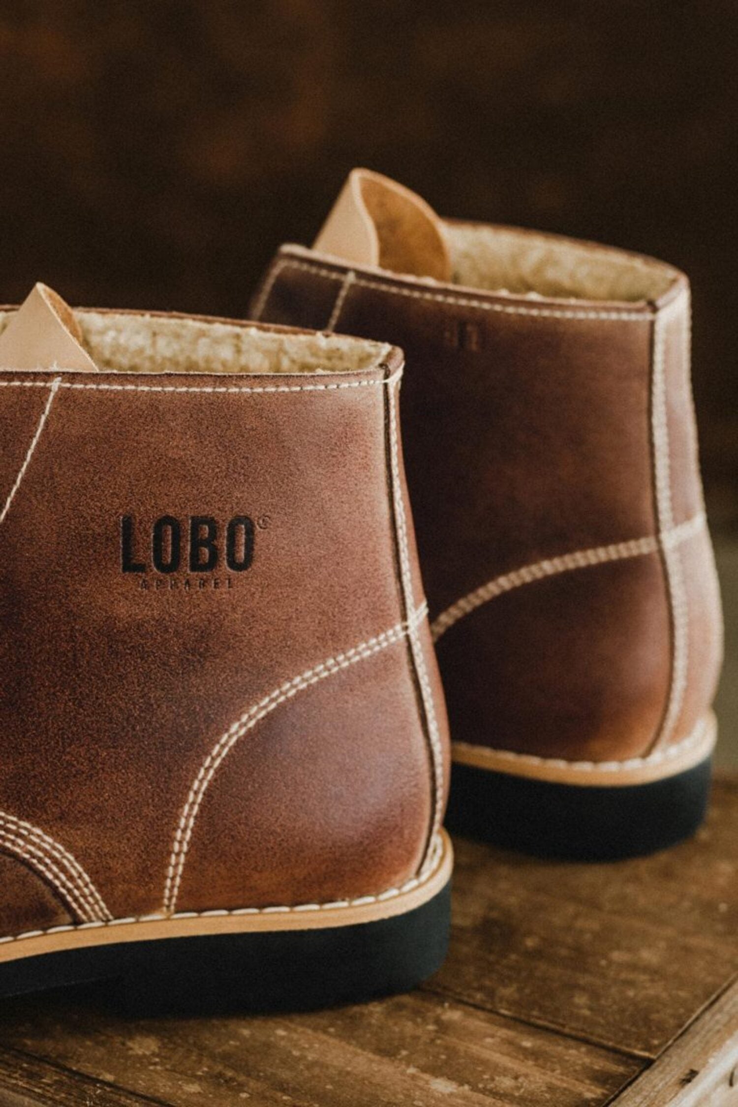 Close-up of the Lobo Apparel logo embossed on the side heel of the brown leather boots.