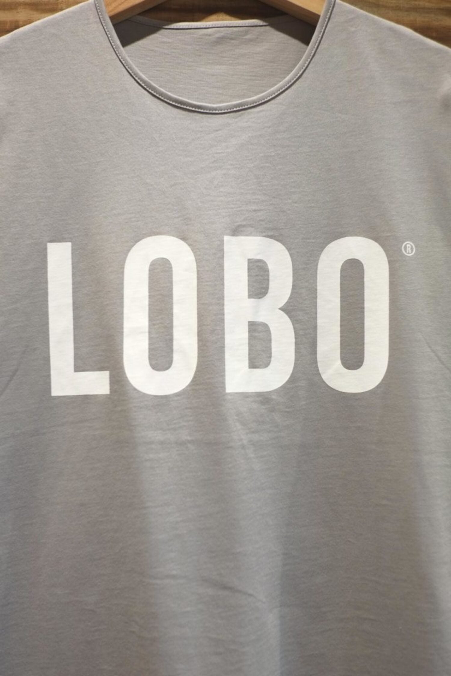 Close-up of the white screen-printed LOBO logo on the chest of the grey t-shirt, highlighting the crew neck and premium cotton texture.