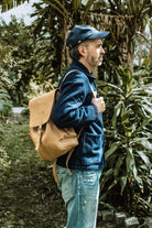Man wearing the Lobo x Naked Malt leather backpack in profile, styled with a blue denim jacket, in a tropical forest background.
