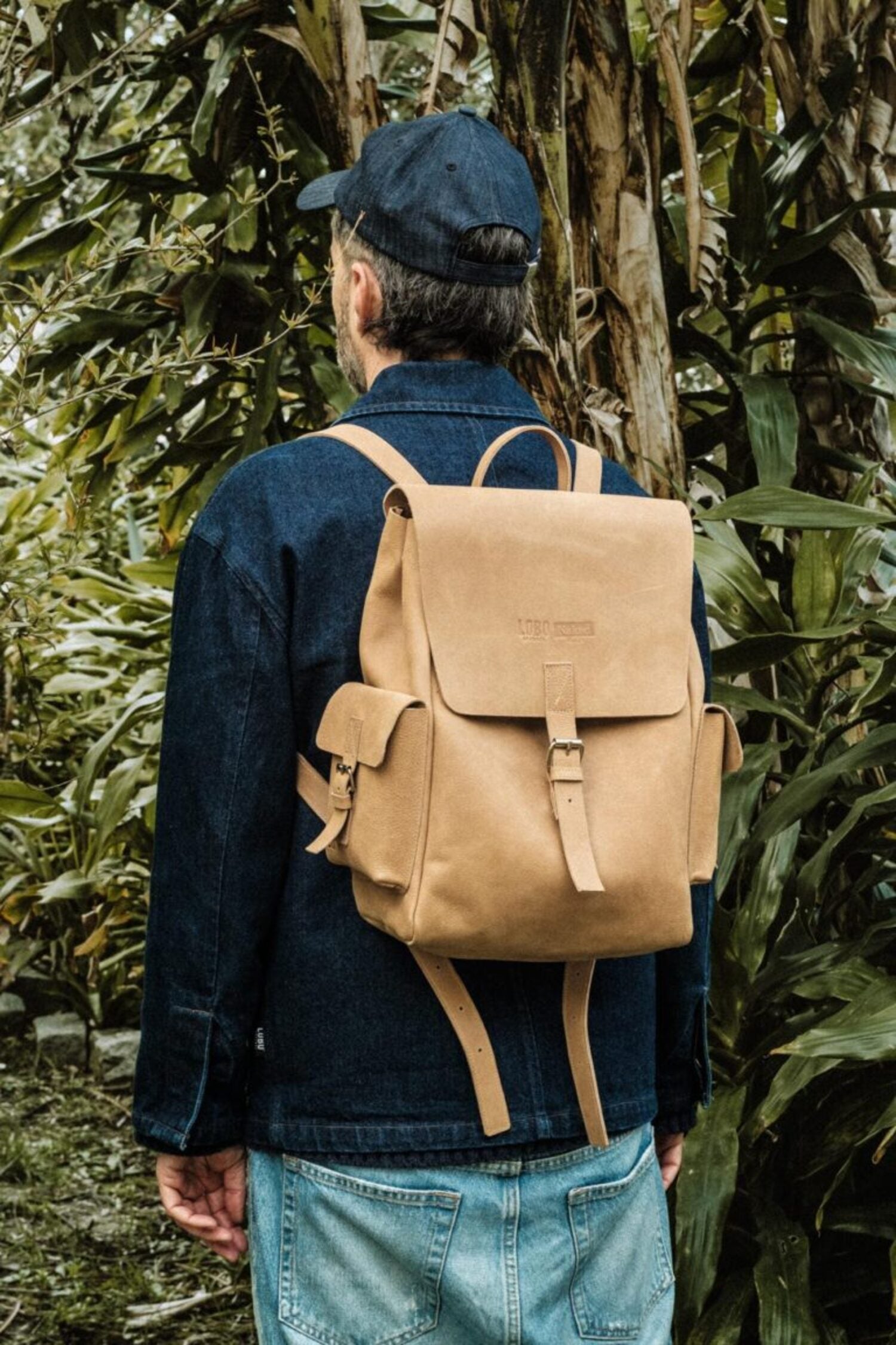 Back view of a male model wearing the Lobo x Naked Malt backpack, highlighting leather straps and structured everyday design.