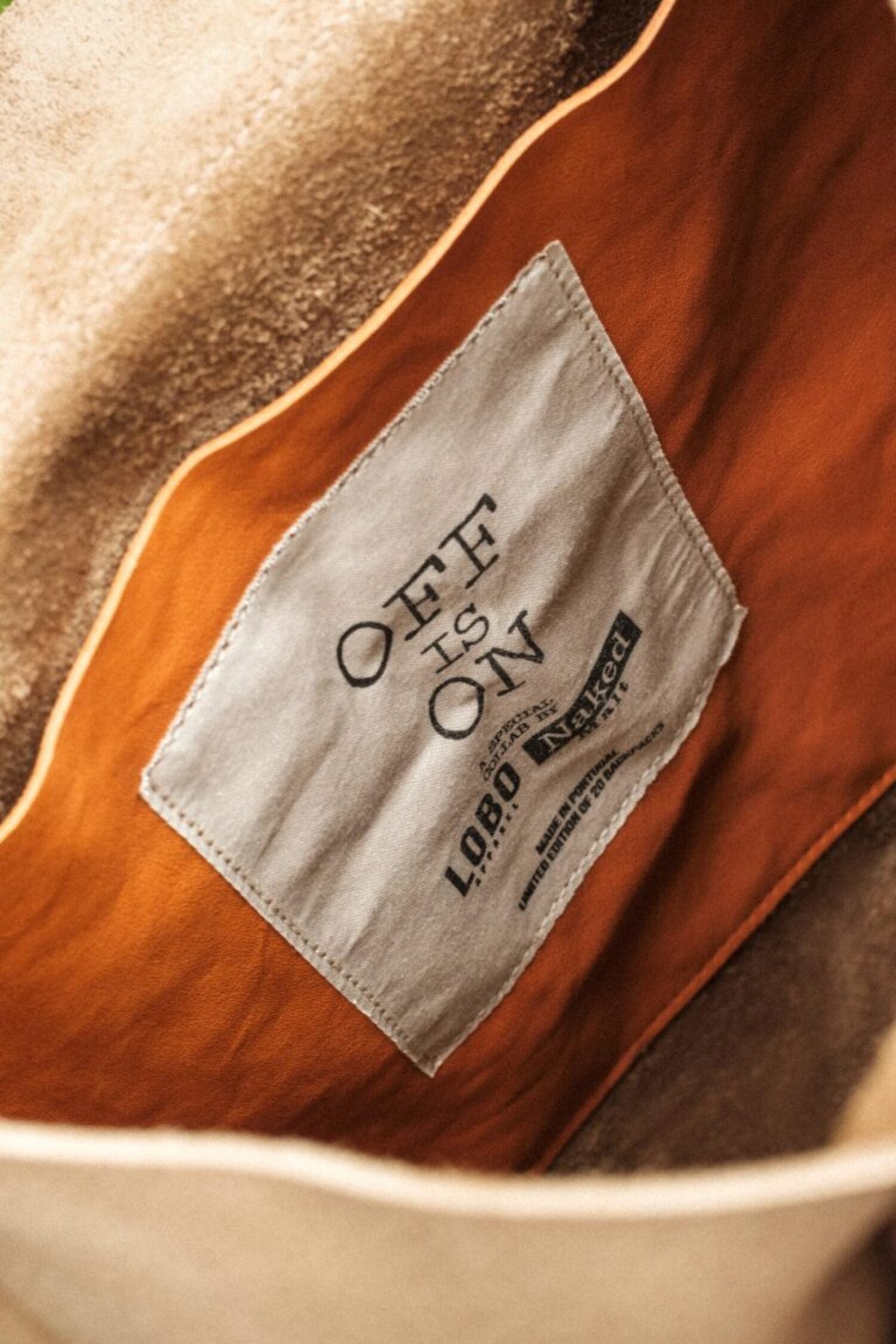 Interior detail of the Lobo x Naked Malt backpack featuring orange lining and "OFF IS ON" woven label, limited edition made in Portugal.