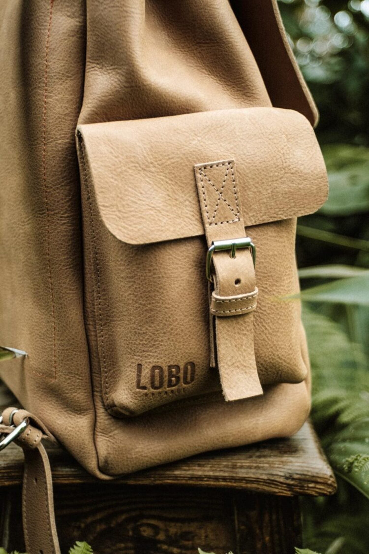 Close-up of the Lobo leather backpack side pocket, featuring premium grain leather, metal buckle, and embossed logo.