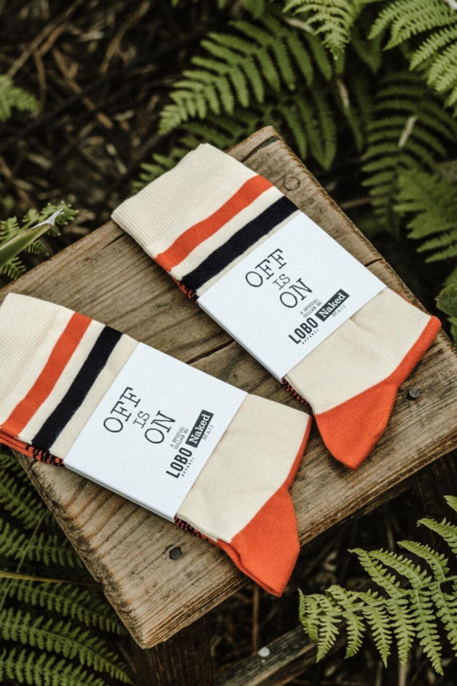 Two pairs of Lobo x Naked Malt collaboration socks folded on a wooden surface, featuring orange and navy stripes with "OFF IS ON" packaging.
