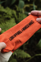 Hands stretching a vibrant orange Lobo Apparel x Naked Malt collaboration sock, highlighting the premium knit texture.