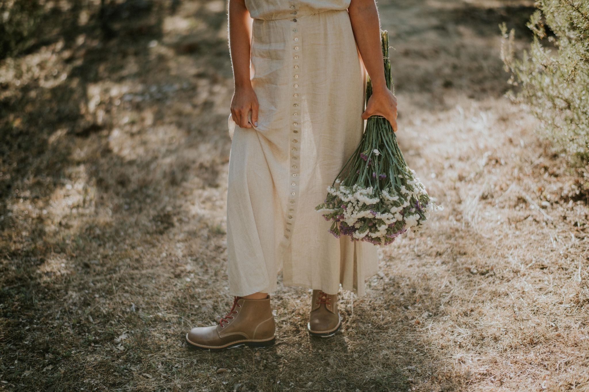 Woman in a field holding wildflowers, wearing brown leather Lobo Raw Boots with red laces.