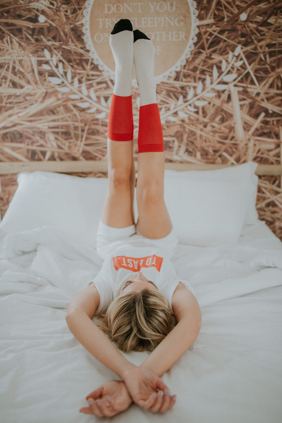 Woman lying on a bed with legs up, wearing white and red Lobo Classic Red Socks.