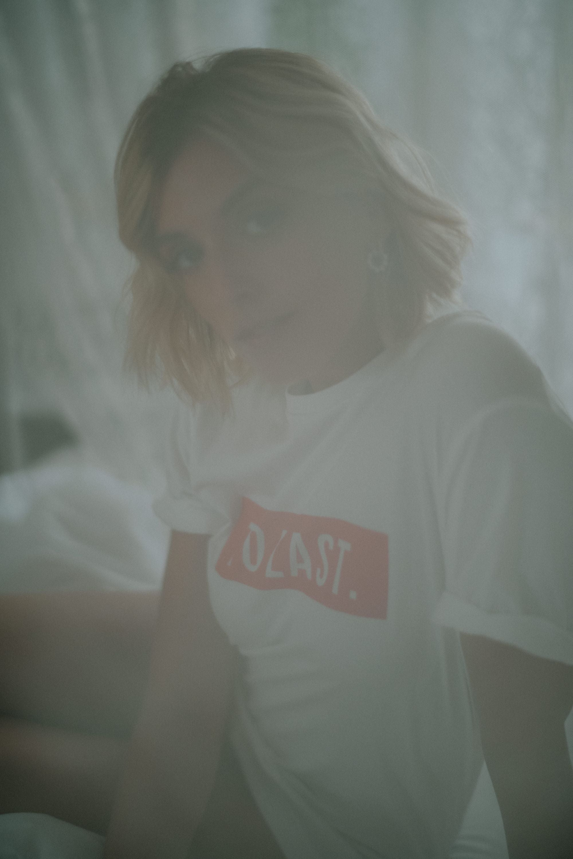 Artistic portrait of a blonde woman wearing the white Lobo Too Last t-shirt, with a soft and blurred lighting effect.