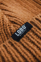 Close-up of the brown wool knit texture of the Manuel Brown Beanie, featuring the black woven label with the Lobo Apparel logo.