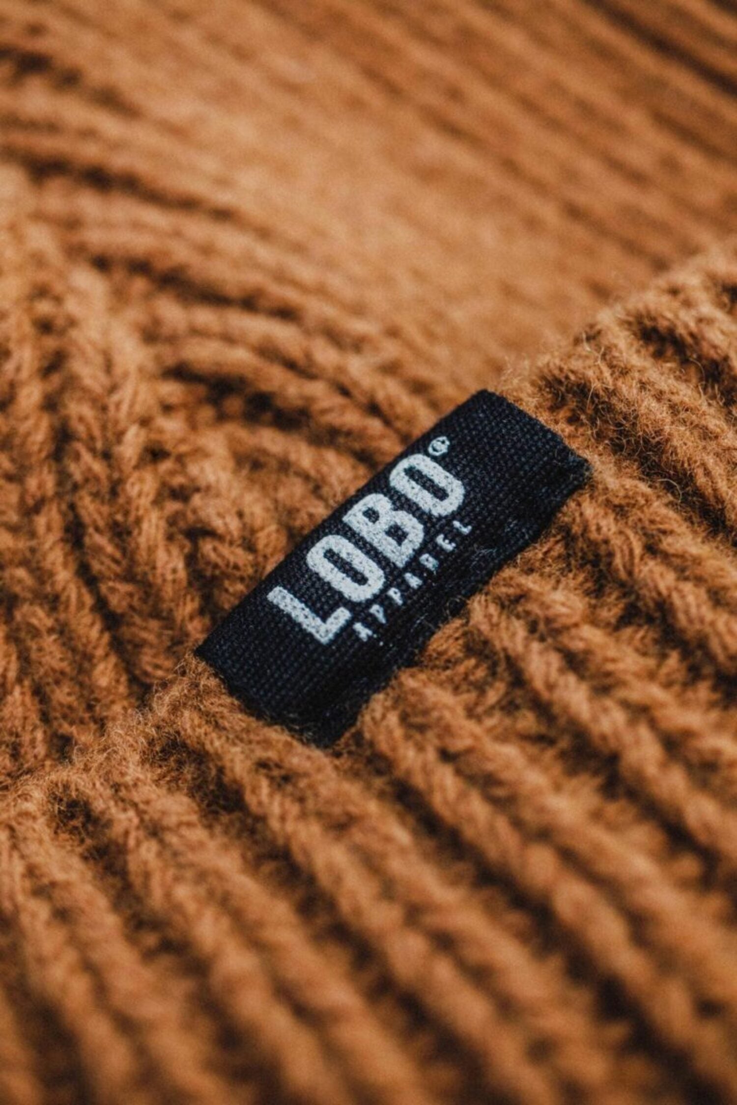 Close-up of the brown wool knit texture of the Manuel Brown Beanie, featuring the black woven label with the Lobo Apparel logo.