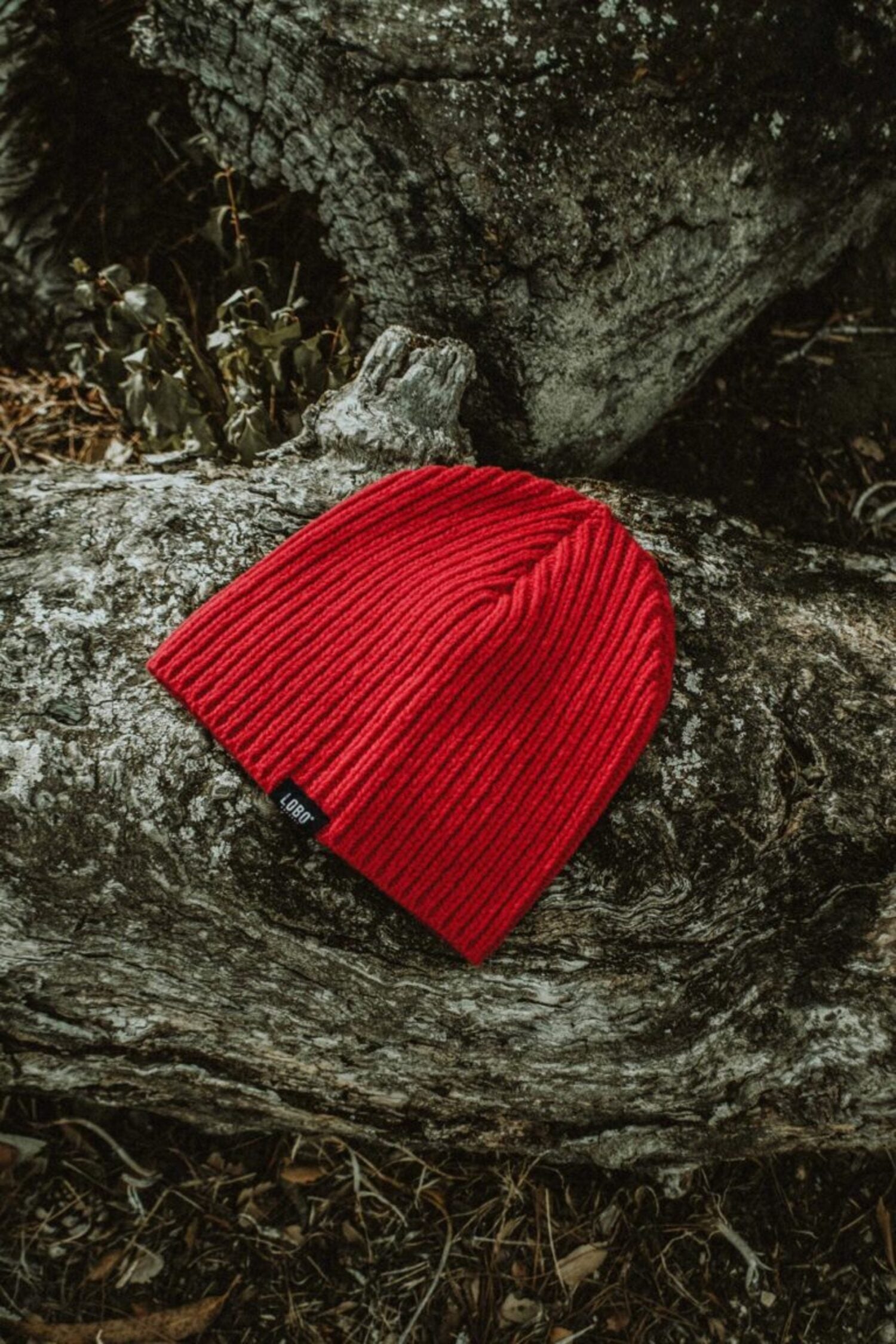 Unisex Manuel Red Beanie in vibrant red, inspired by traditional fisherman style, placed on rustic wood.