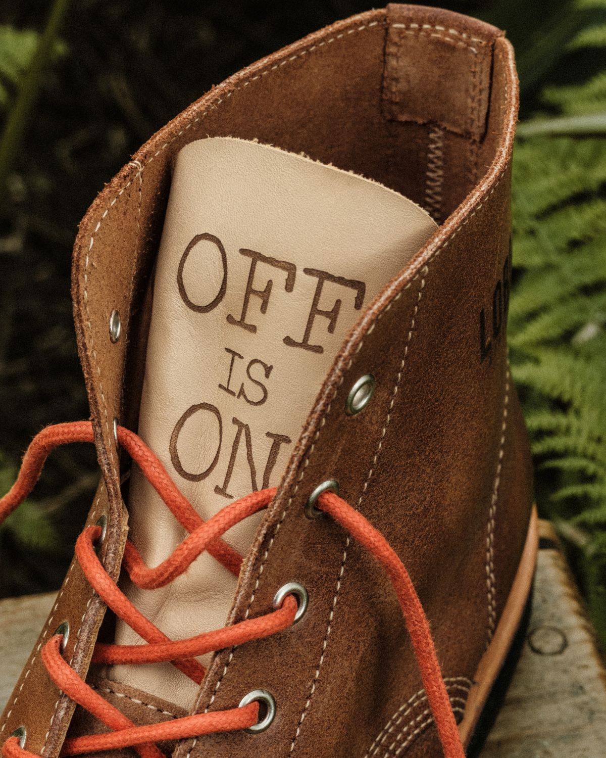 Close-up of the Lobo x Naked Malt Collab Raw Boots shaft, highlighting the "OFF IS ON" phrase engraved on the light leather tongue and the orange laces.