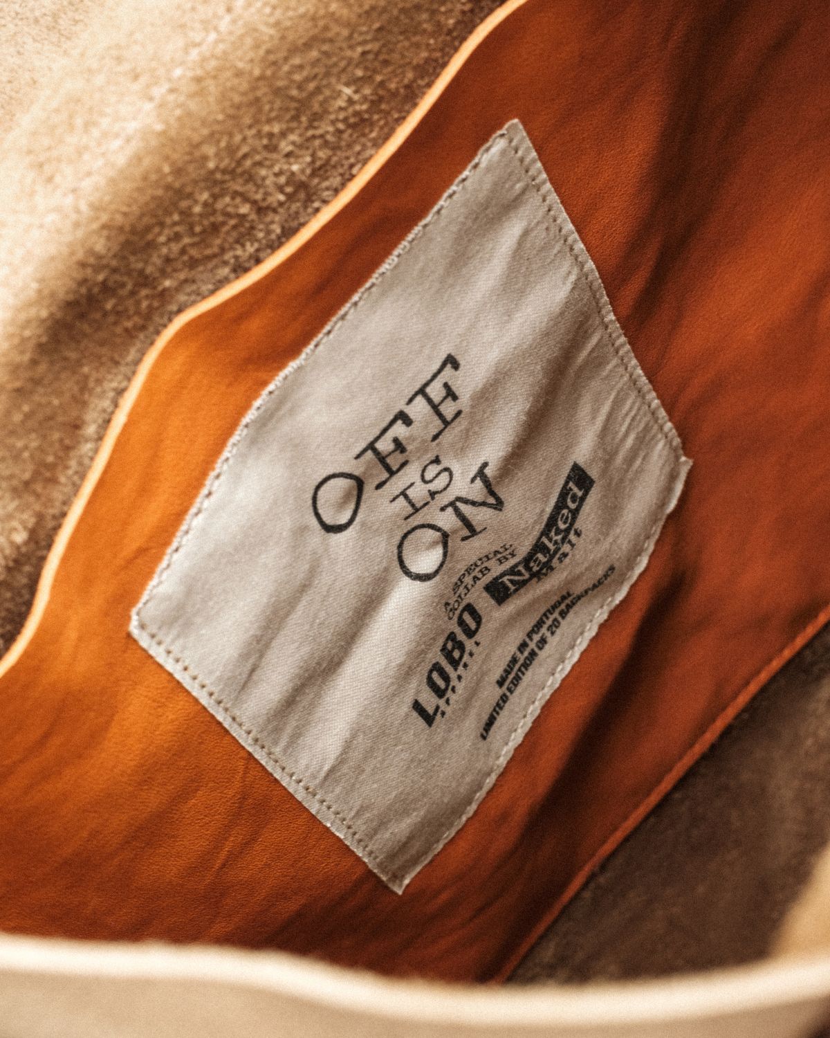 Close-up of the interior of the Lobo x Naked Malt Collab Backpack, showing the fabric label with the phrase "OFF IS ON", the brand logos, and the information "Made in Portugal - Limited Edition"