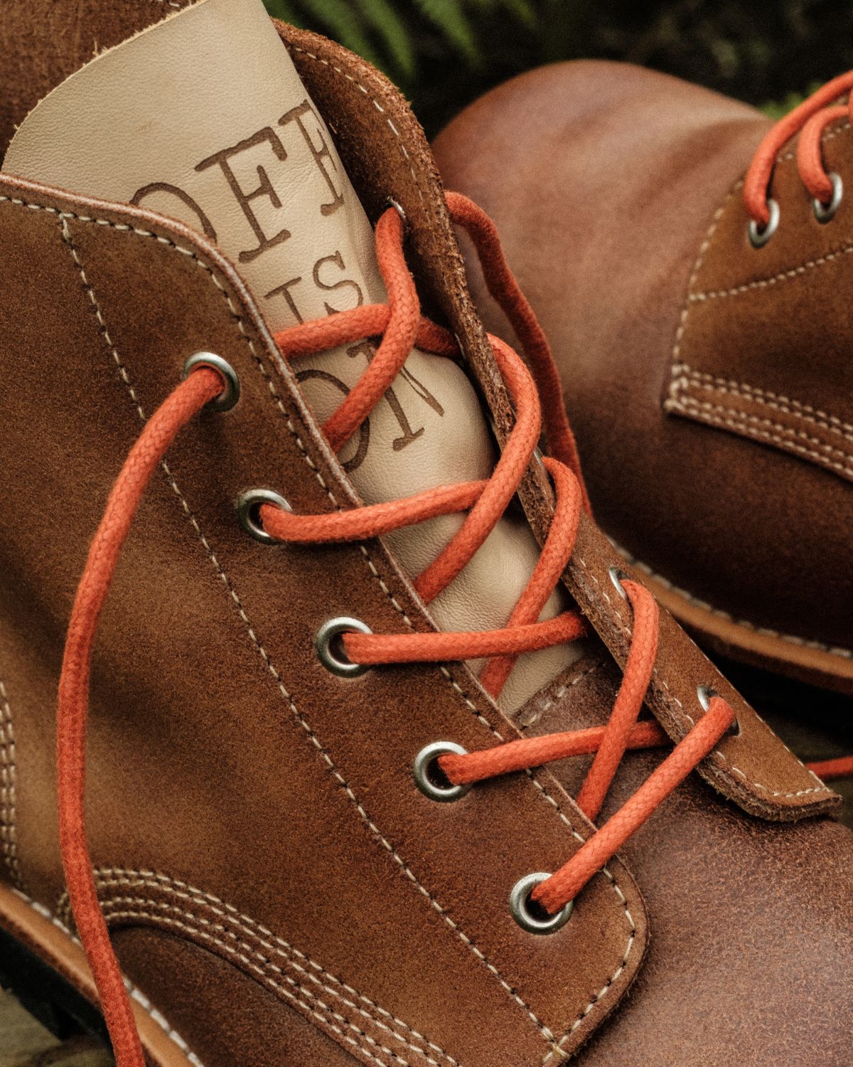 Close-up of Lobo x Naked Malt brown leather boots with orange laces and "OFF IS ON" text on the tongue, made in Portugal.