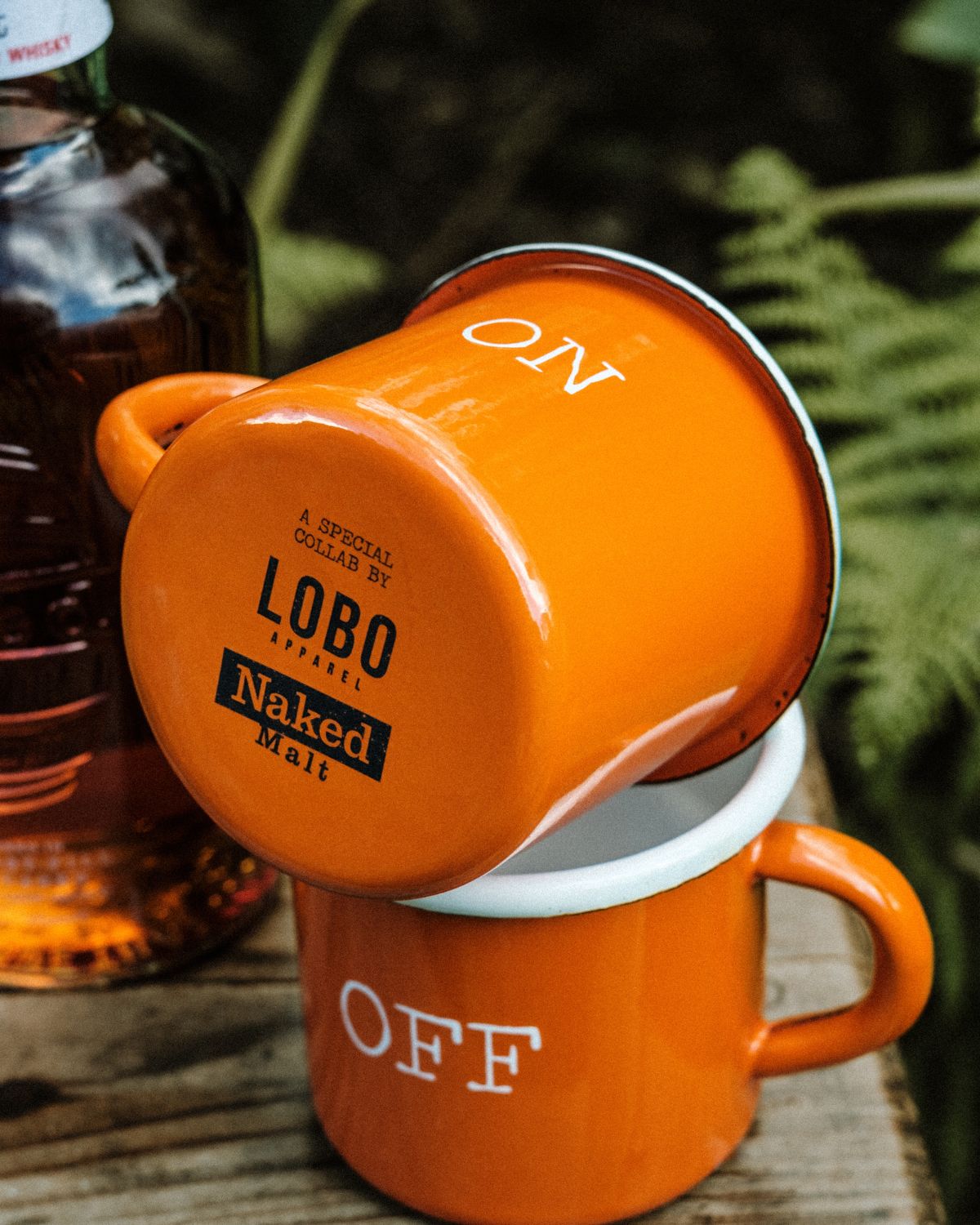 Close-up of two orange Lobo x Naked Malt Collab Enamel Mug, focusing on the collaboration logos printed on the bottom and the words "ON" and "OFF".