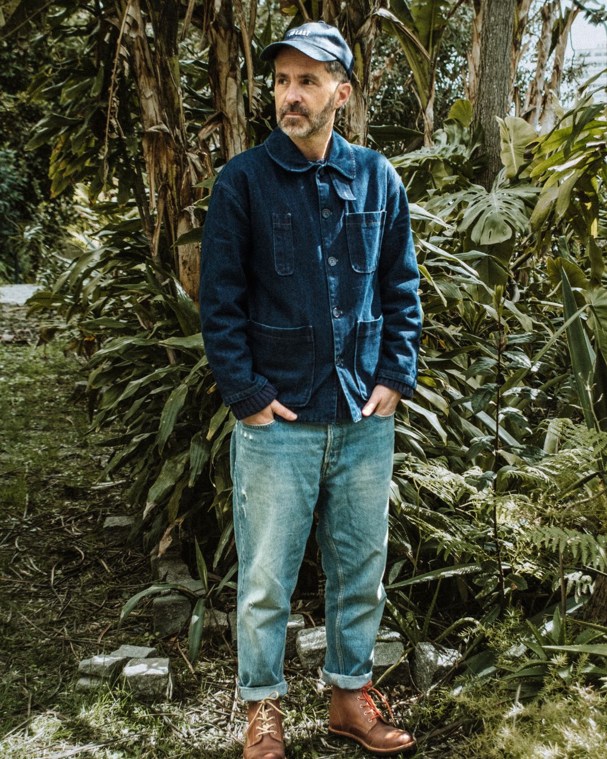 Man in an outdoor setting wearing the full collection look, featuring the Lobo x Naked Malt Collab Raw Boots in brown leather with orange laces, blue jacket, and denim jeans.