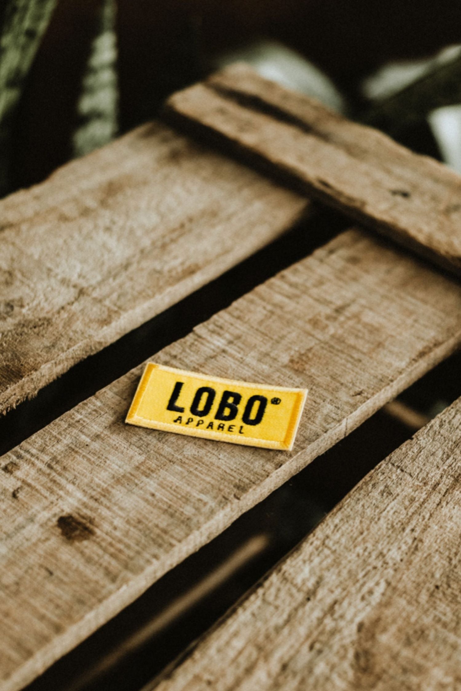 Yellow Lobo Apparel embroidered logo patch on a rustic wooden surface, representing the brand's identity.