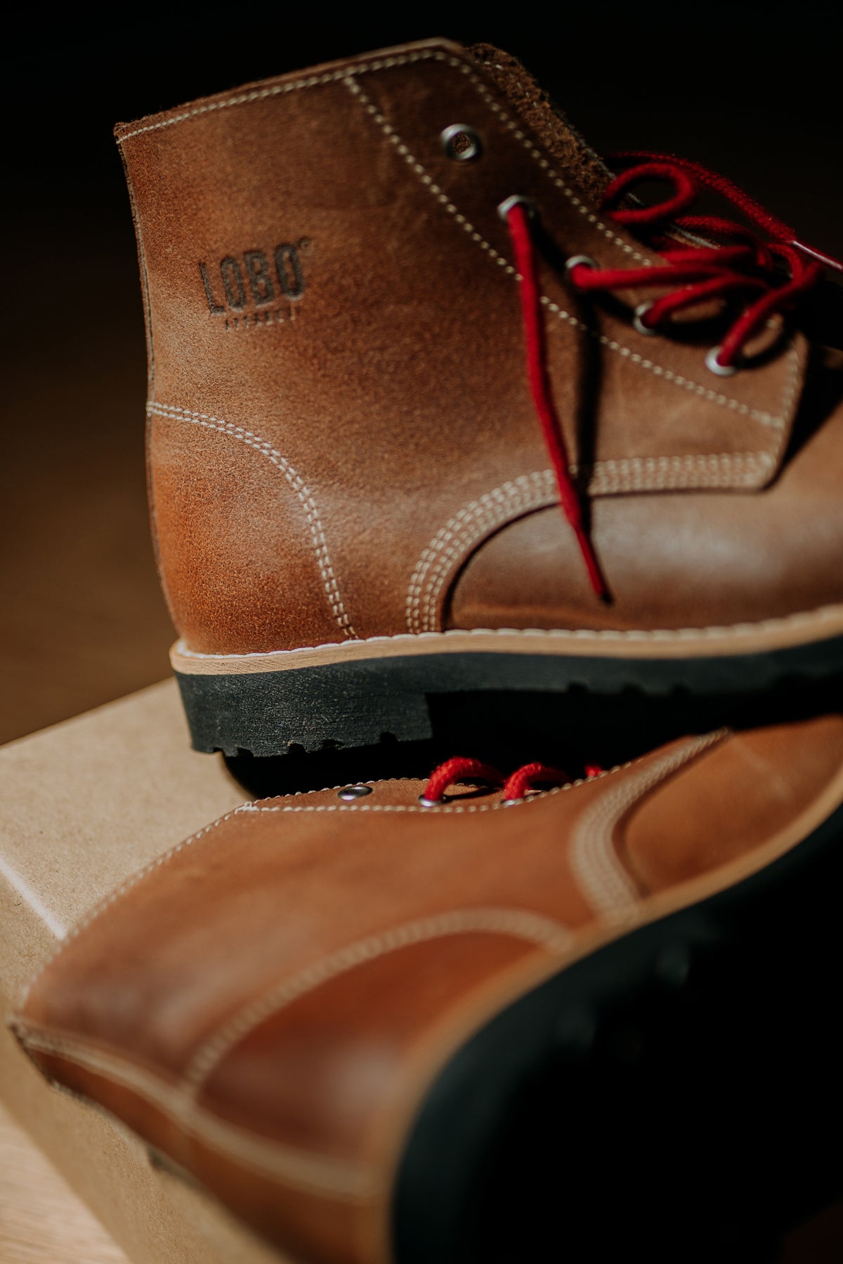 Close-up of the heel of the brown leather Lobo Raw Boots, showing the sturdy black sole, detailed white stitching, and vibrant red laces.