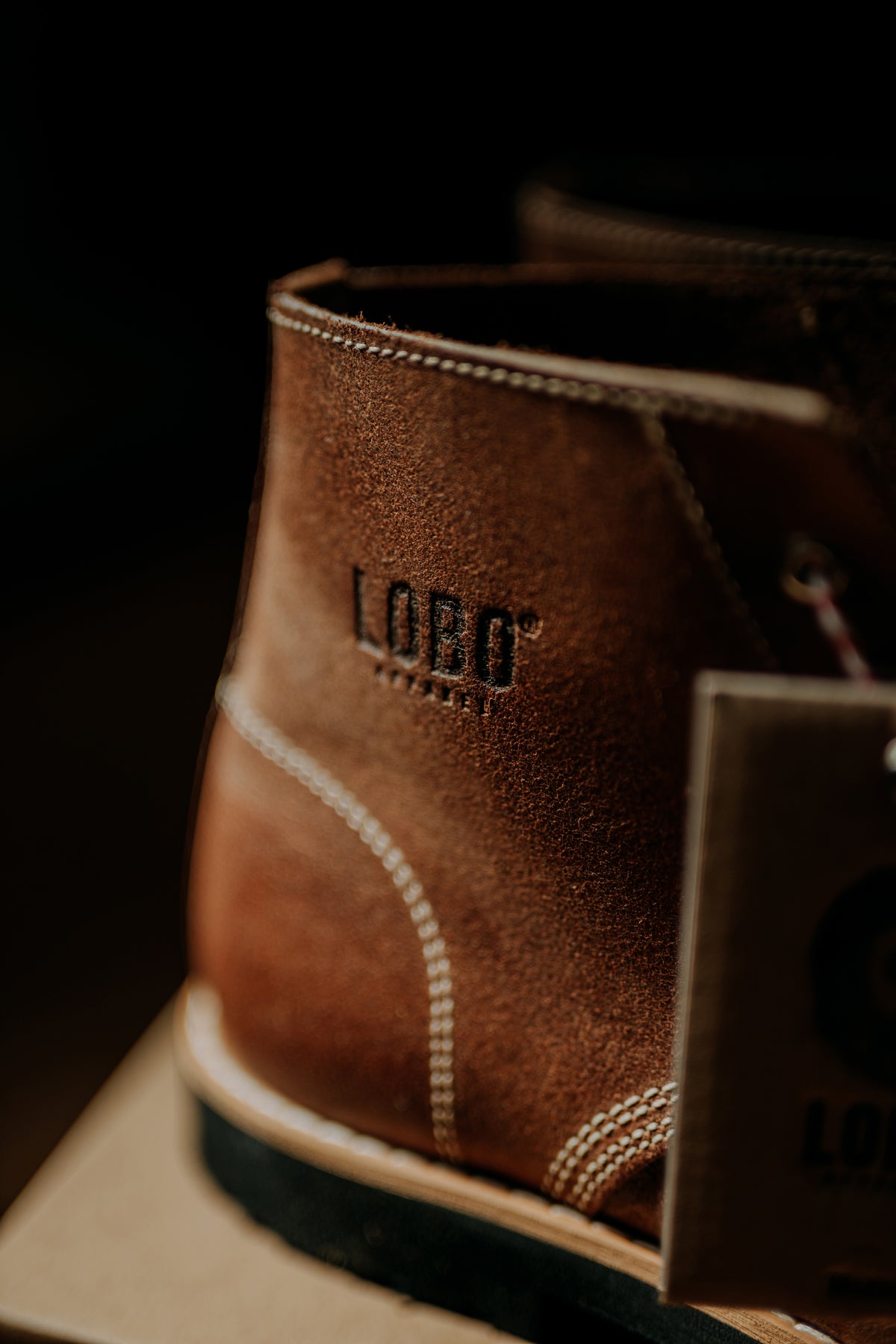 Close-up of the side of the Lobo Raw Boots boot, highlighting the debossed LOBO logo on the leather and the contrasting white stitching.