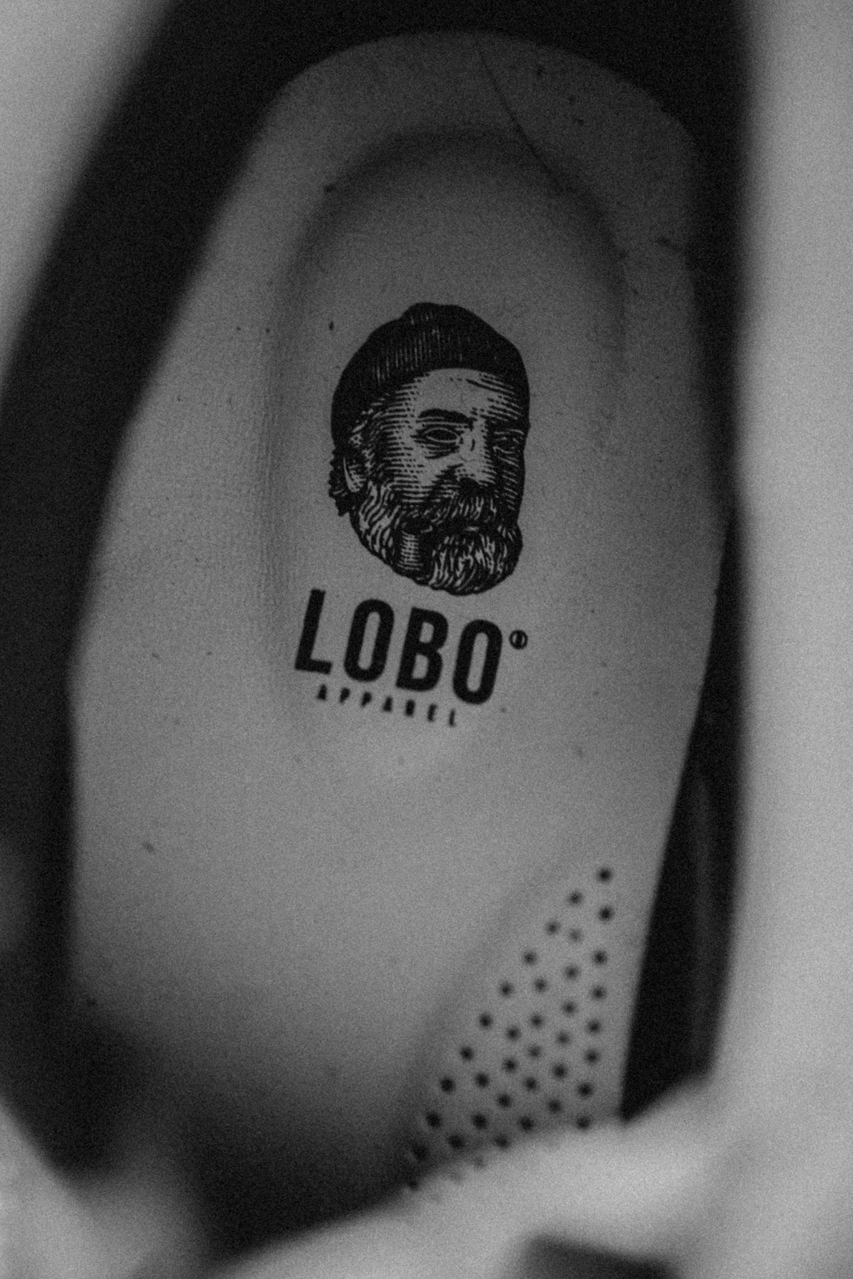 Detail of the interior of the Lobo Raw Boots, focusing on the insole with the printed logo of a bearded man wearing a beanie and a pipe above the name LOBO Apparel.