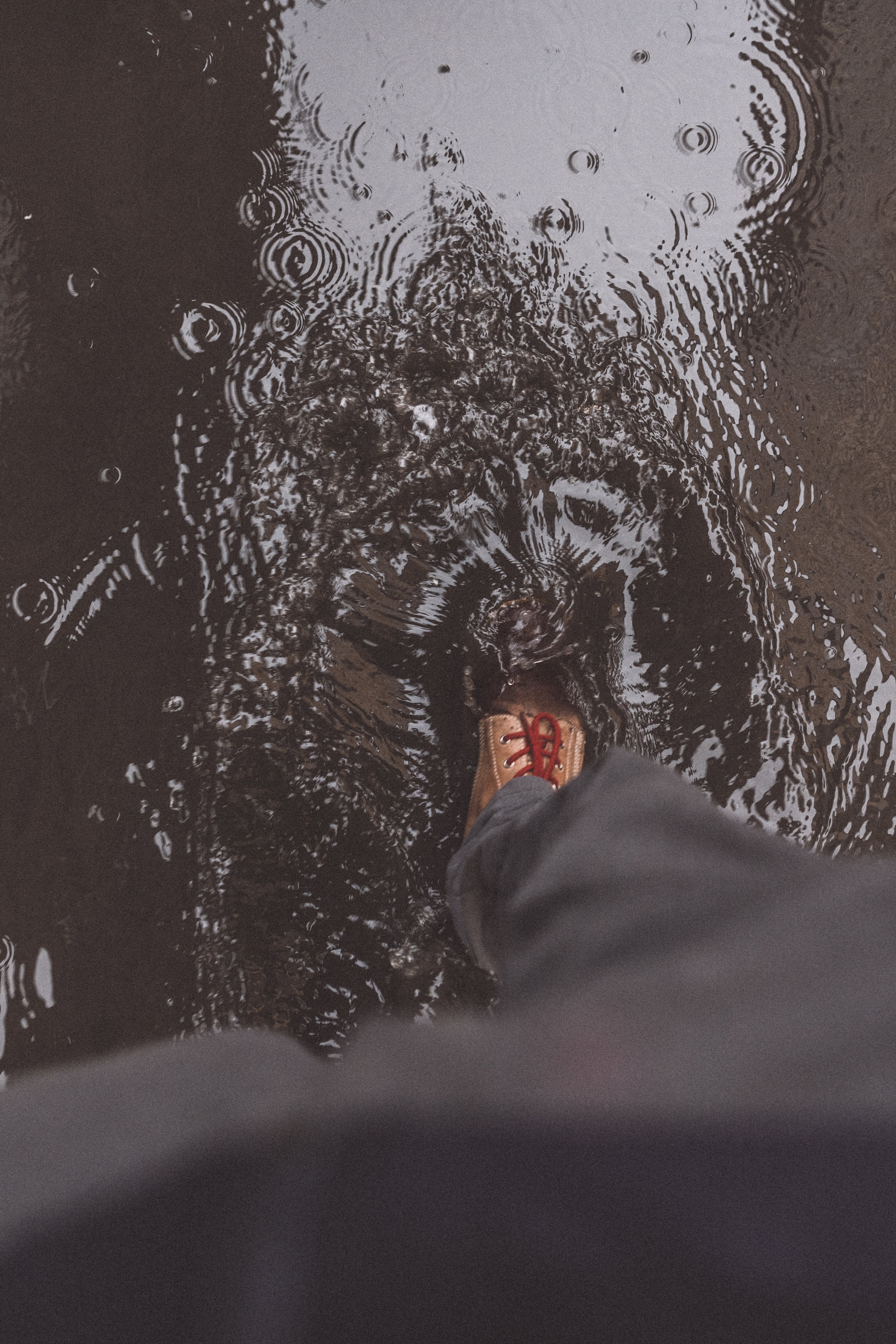 First-person view of a Lobo Raw Boots boot stepping into a puddle, creating ripples and demonstrating the footwear's resistance on wet terrain.
