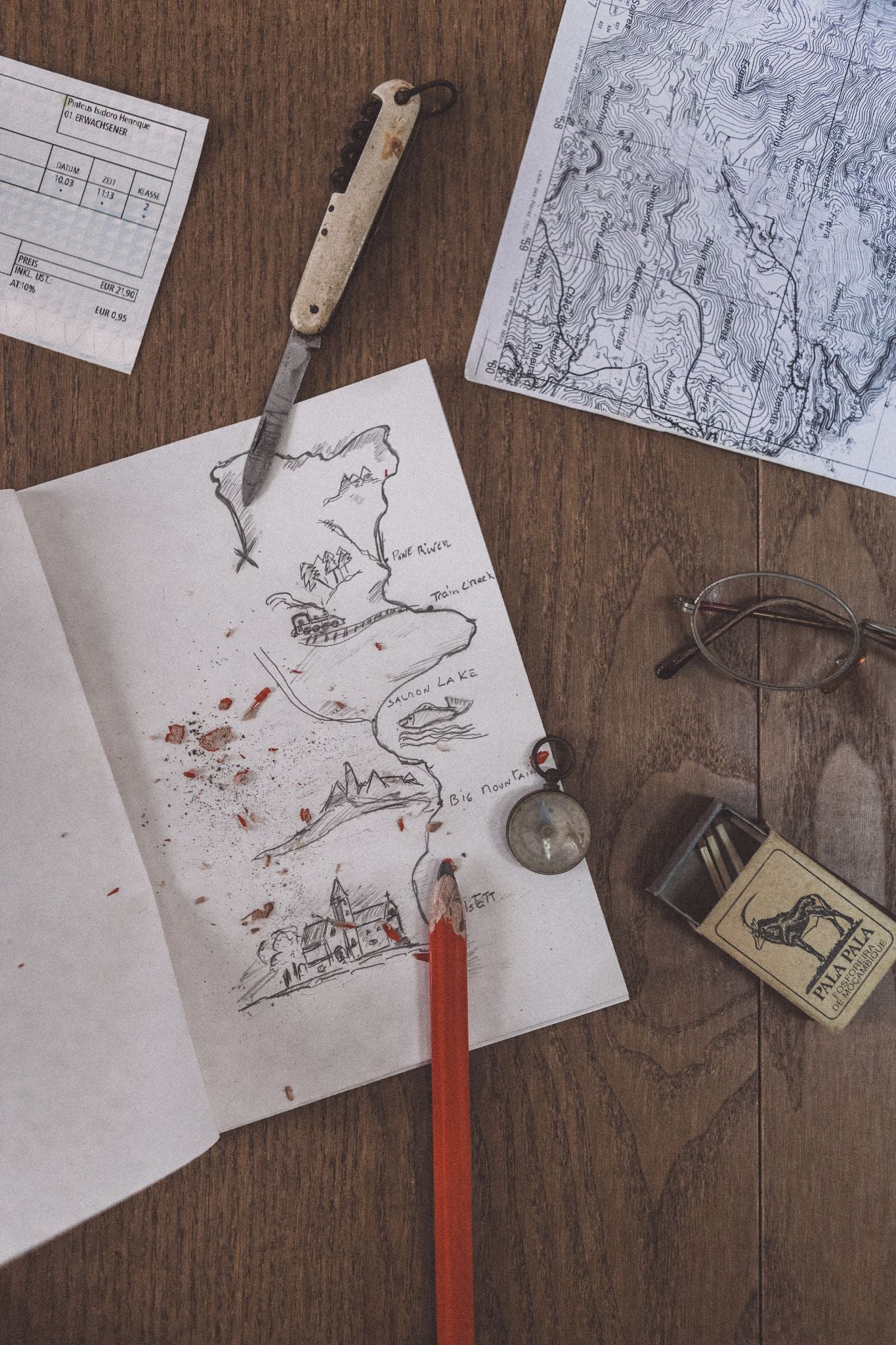 Rustic table with a hand-drawn map in a notebook, glasses, compass, pocket knife, and matches, evoking the adventure spirit of the Lobo brand.