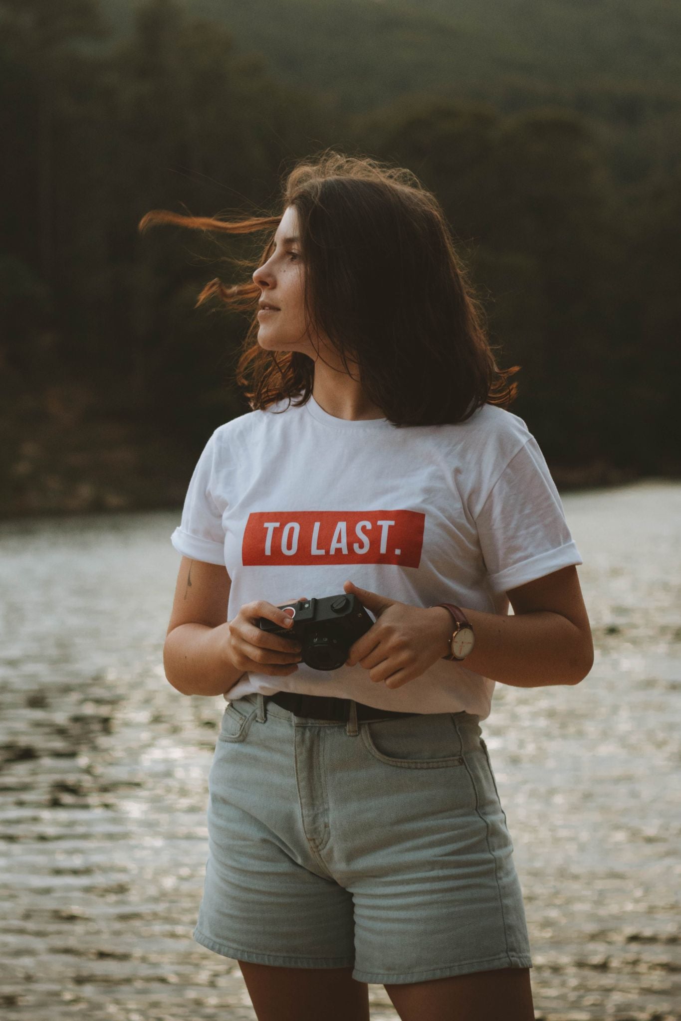 Outdoor portrait of a woman holding an analogue camera, wearing the To Last t-shirt at Rio da Mula.