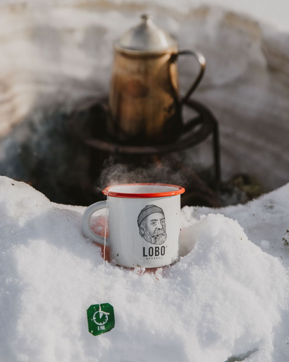 Lobo Enamel Mug with steam from a hot drink, set in a winter survival and comfort scene.