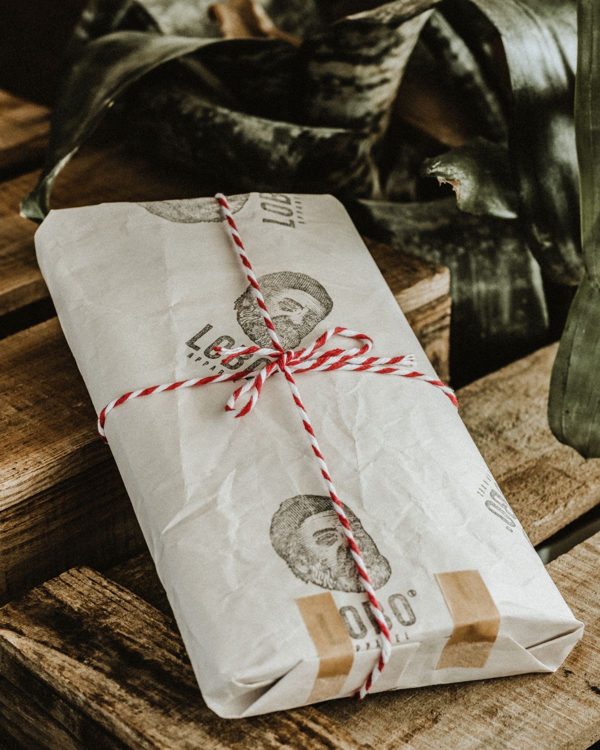 LOBO brand gift packaging, wrapped in white paper featuring the illustrated logo (bearded man) and tied with a rustic red and white twine. Artisanal and premium unboxing experience.