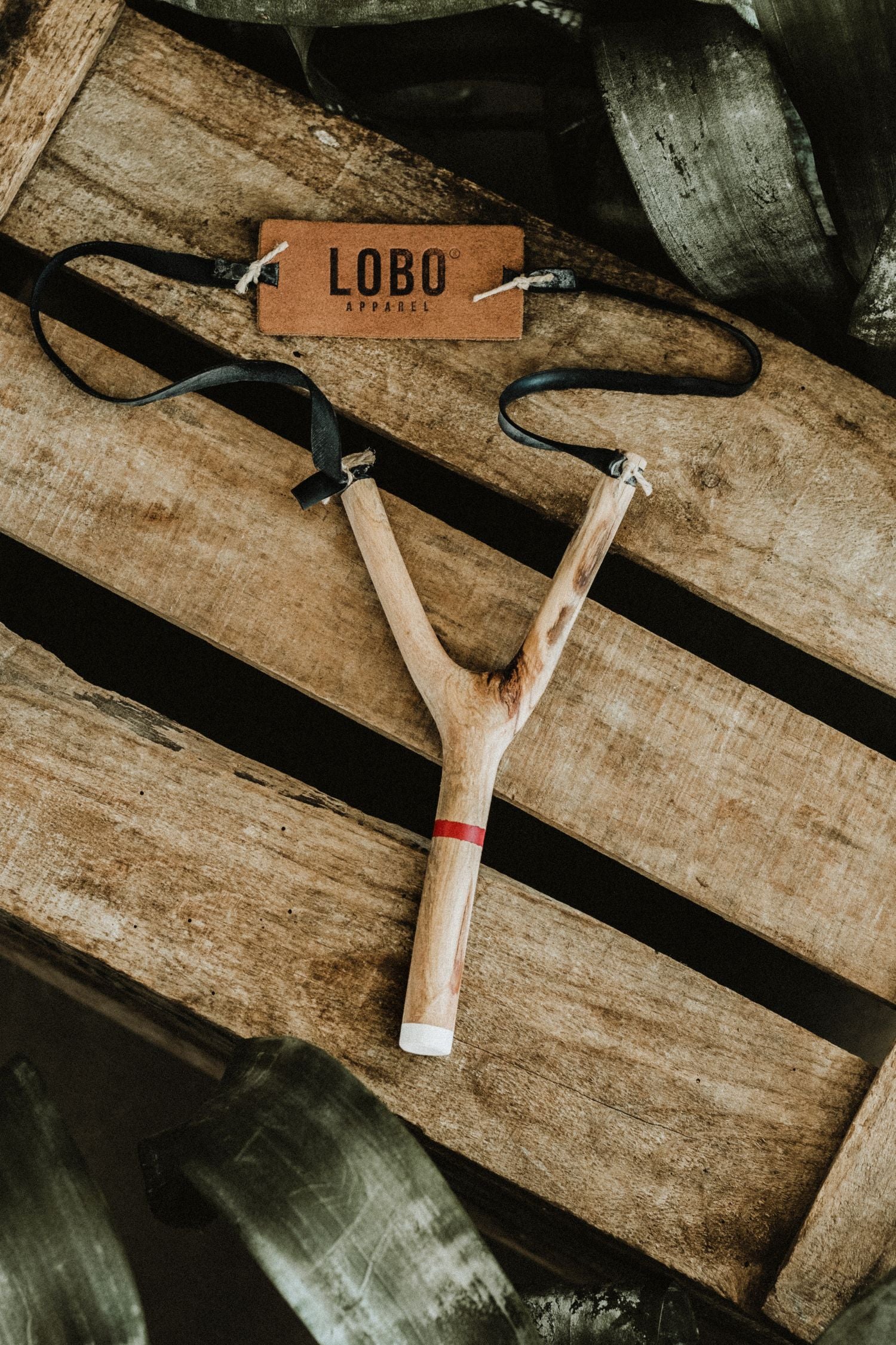 Top view of a limited edition LOBO artisanal slingshot and its embossed leather tag. Hand-carved wooden piece for outdoor moments, Cuscuz Studio collaboration.