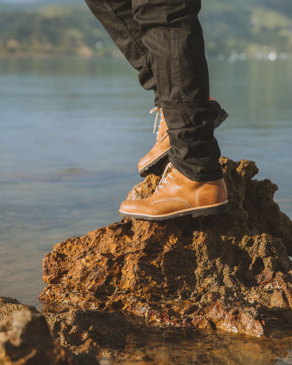 Close-up of brown leather Lobo Raw Boots on a rock by the water.