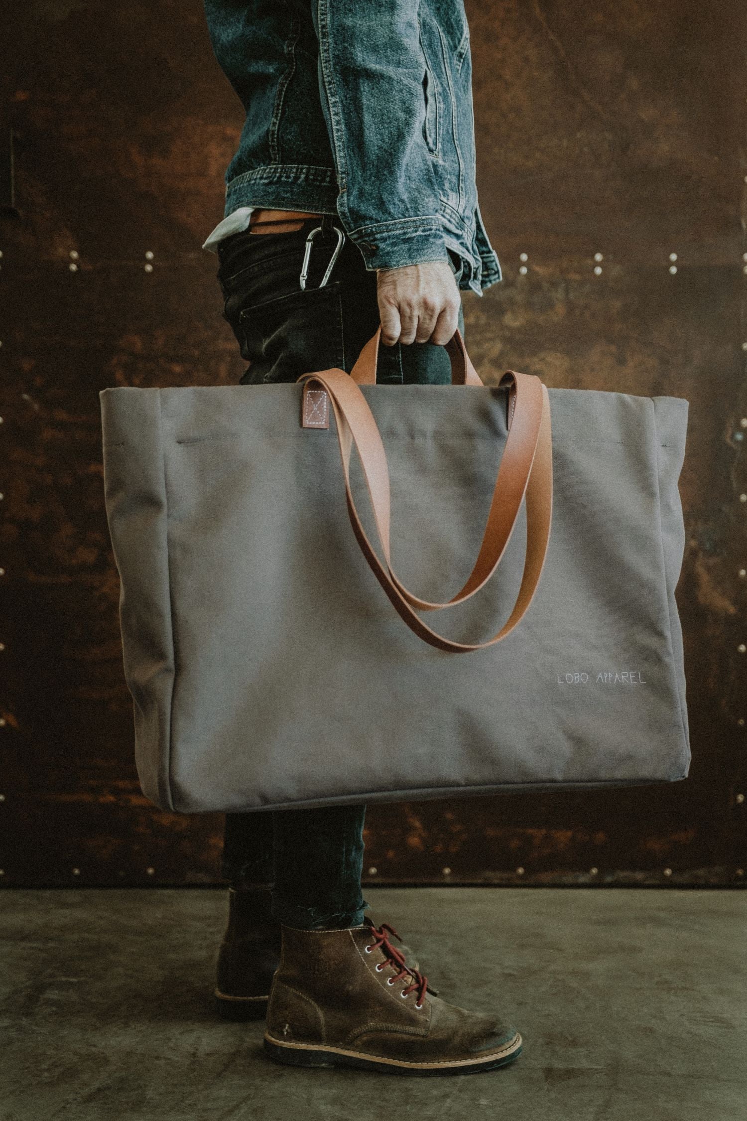 Lobo Apparel XXL bag in military green canvas with natural leather handles, held by hand.
