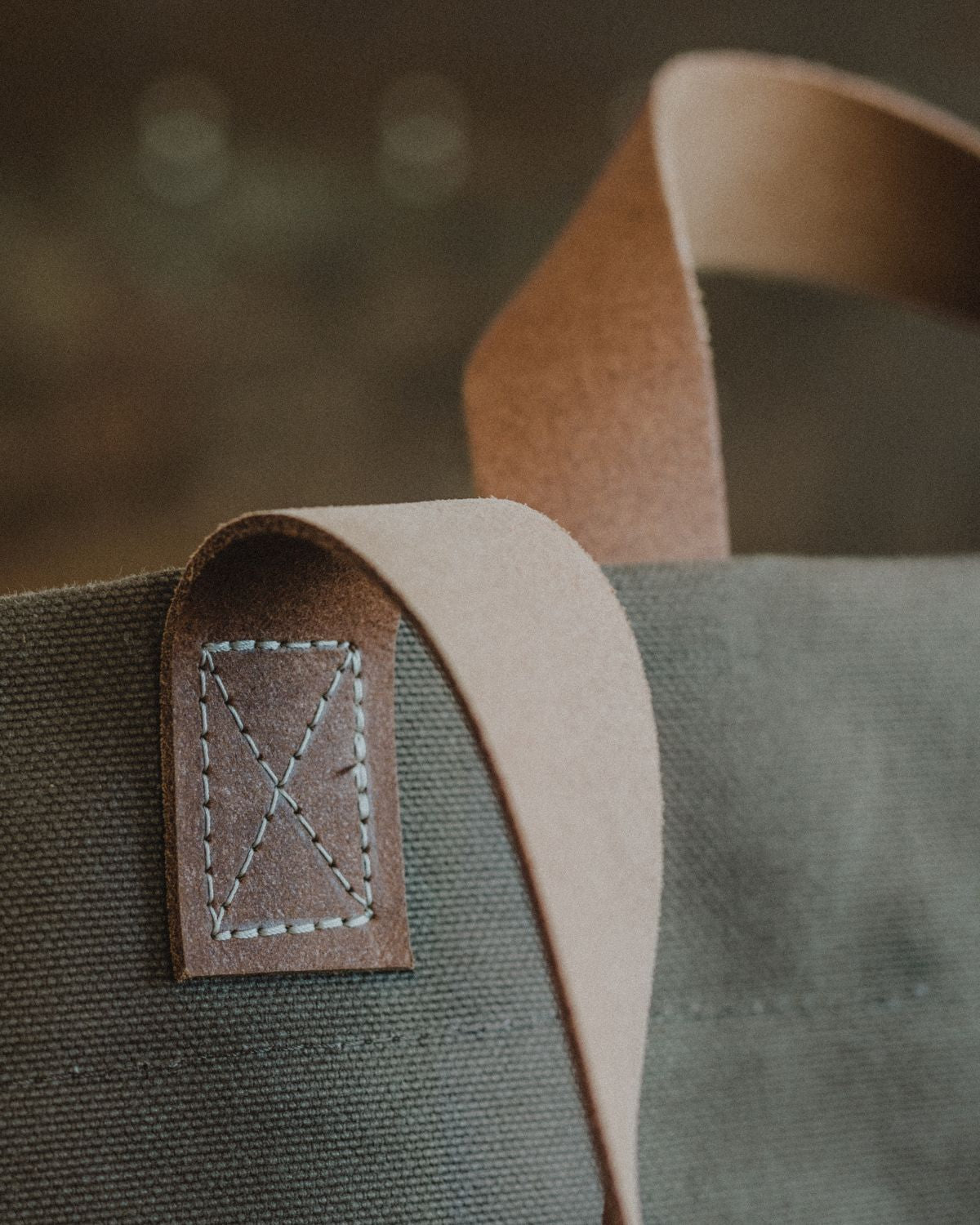 Close-up of the cross-stitch reinforcement on the leather strap of the Lobo Apparel canvas bag, highlighting the handmade craftsmanship.