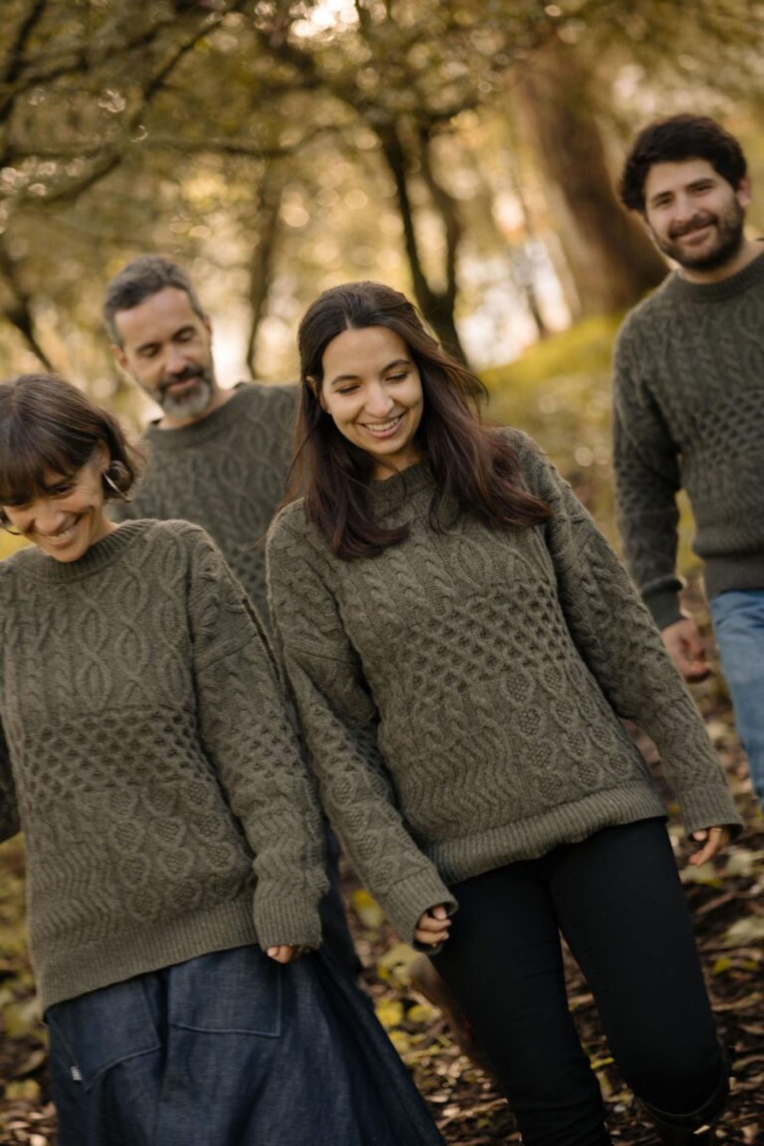 A group of friends smiling in a forest setting, all wearing the "Verde Grisalho" unisex sweater from the Lobo x Do Zero collaboration, made from 100% recycled yarn.