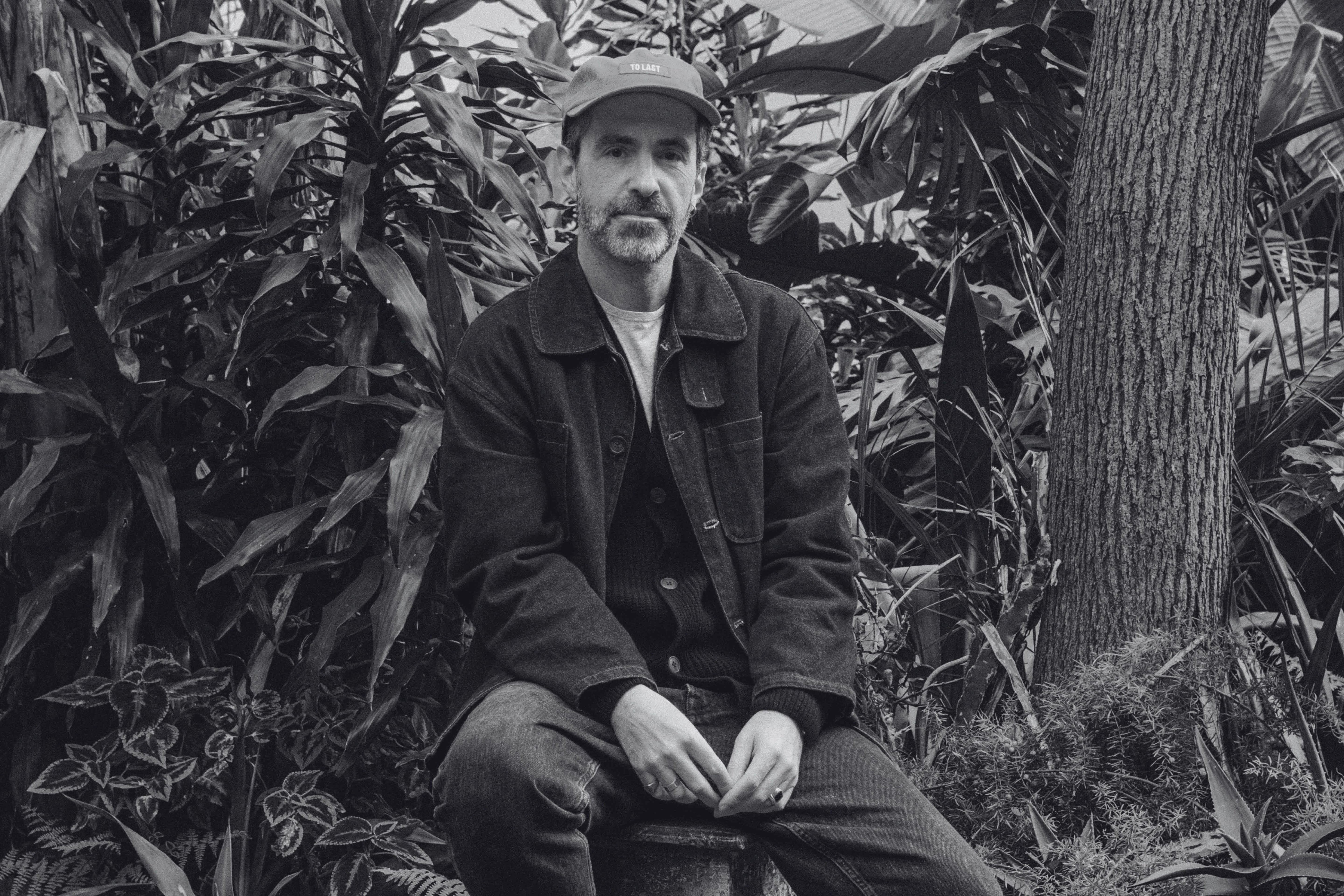 Artistic black and white photograph of Bruno Pereira, founder and creative director of Lobo Apparel, surrounded by natural lush greenery.