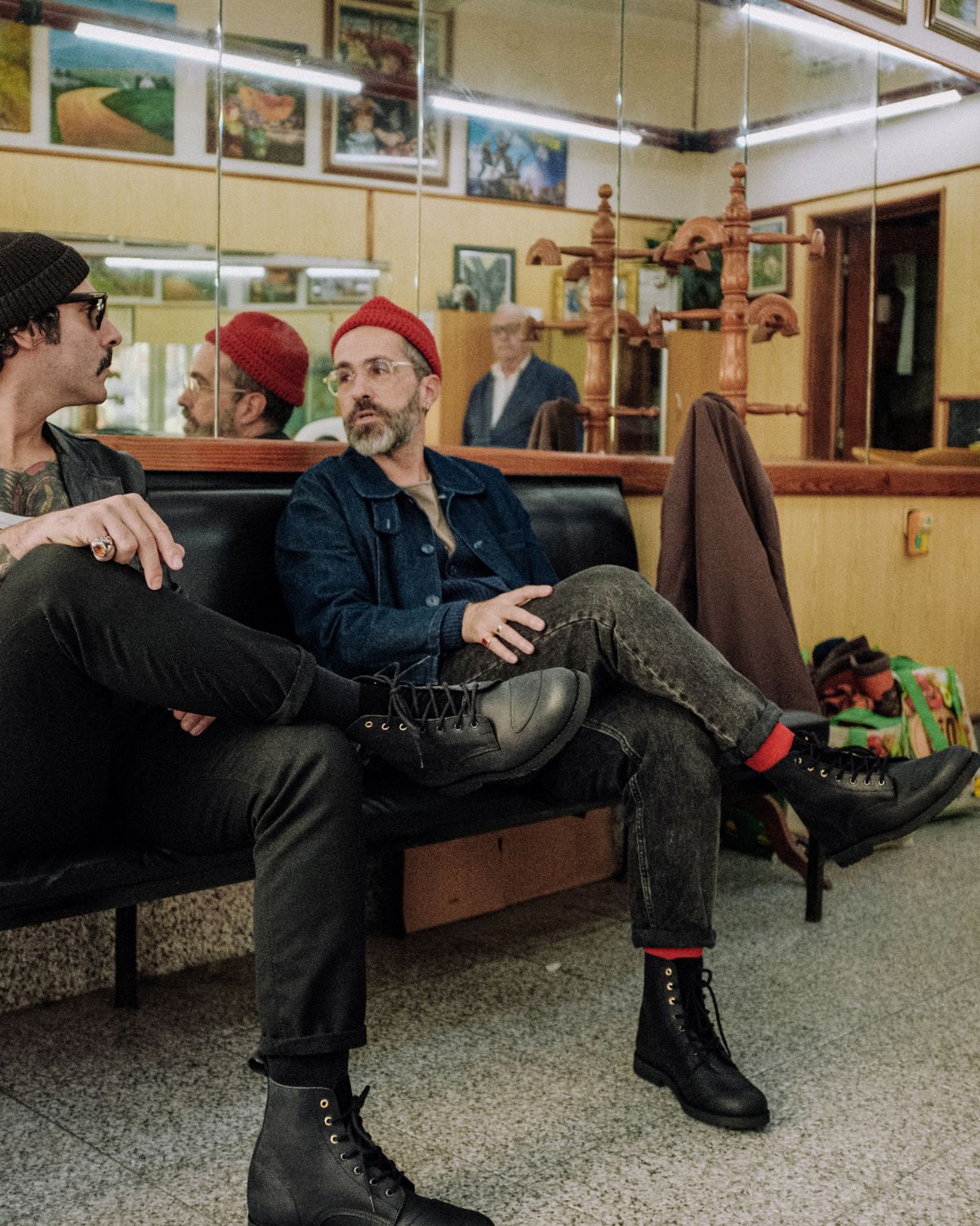 Two men sitting and talking, both wearing the black leather Lobo Tigre Boots, showcasing the footwear's design and flexibility from different angles.