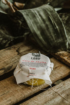 Lobo natural beeswax leather conditioner jar with rustic fabric cover, set on wood in an organic setting.